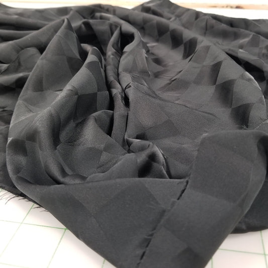 Close-up of black fabric with geometric pattern on a tiled wall background. Designer Deadstock Fabric