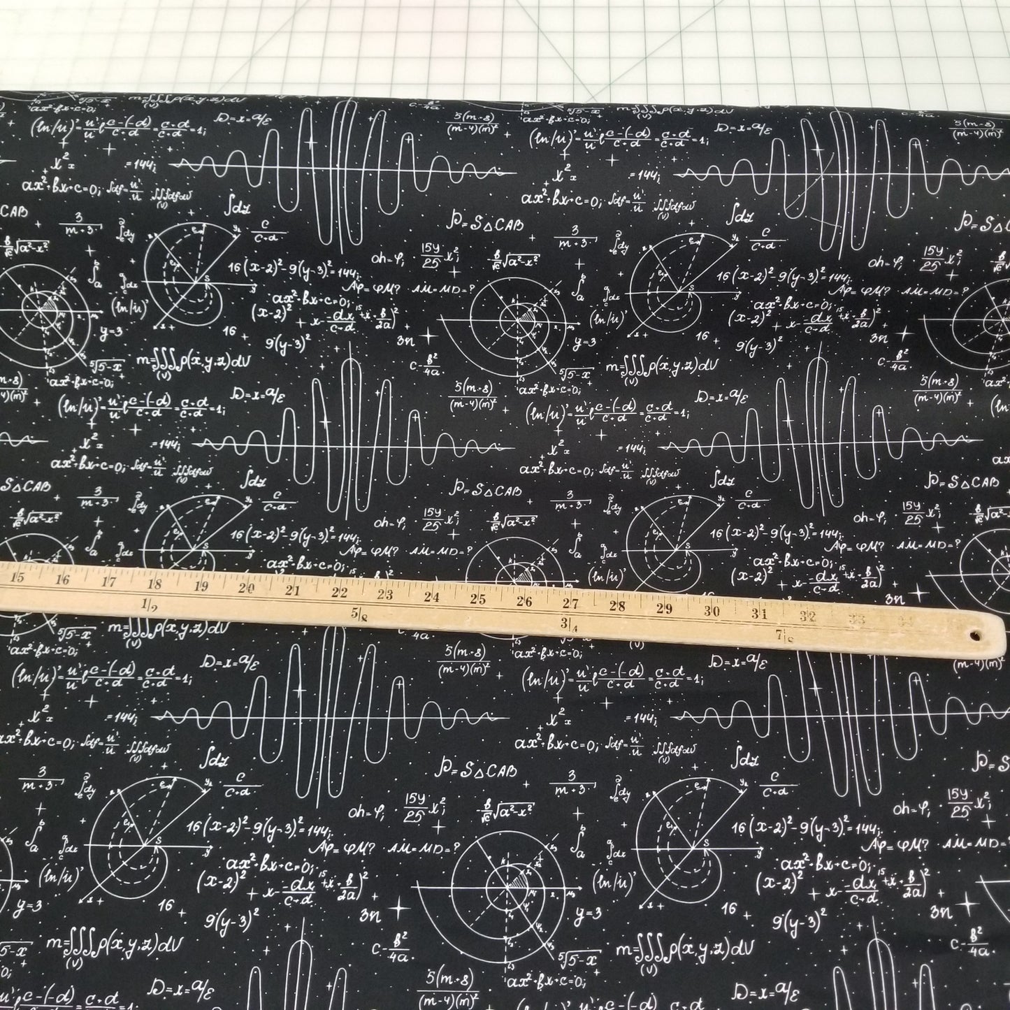 Fabric with mathematical equations and formulas on a black background, measured by a wooden ruler.