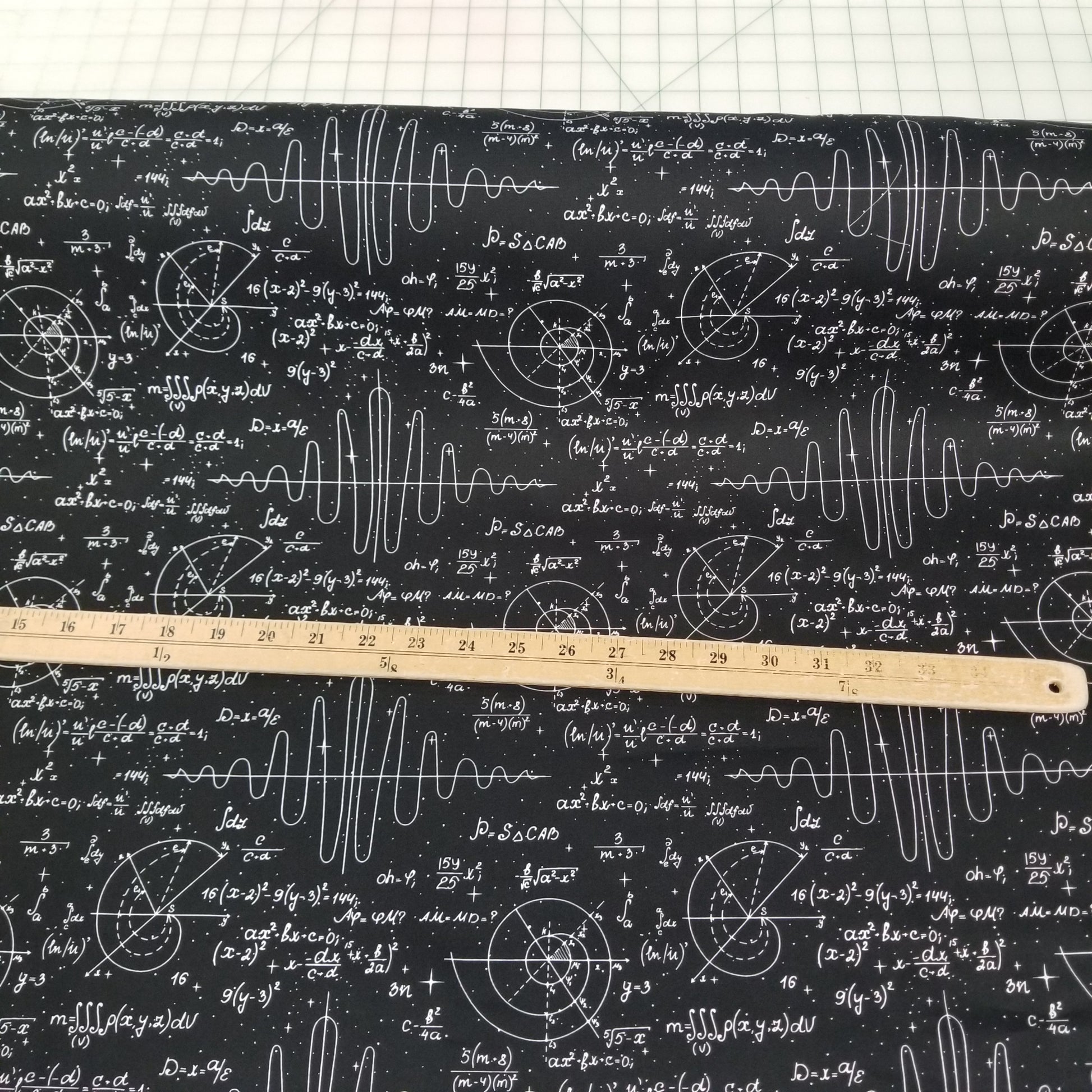 Fabric with mathematical equations and formulas on a black background, measured by a wooden ruler.