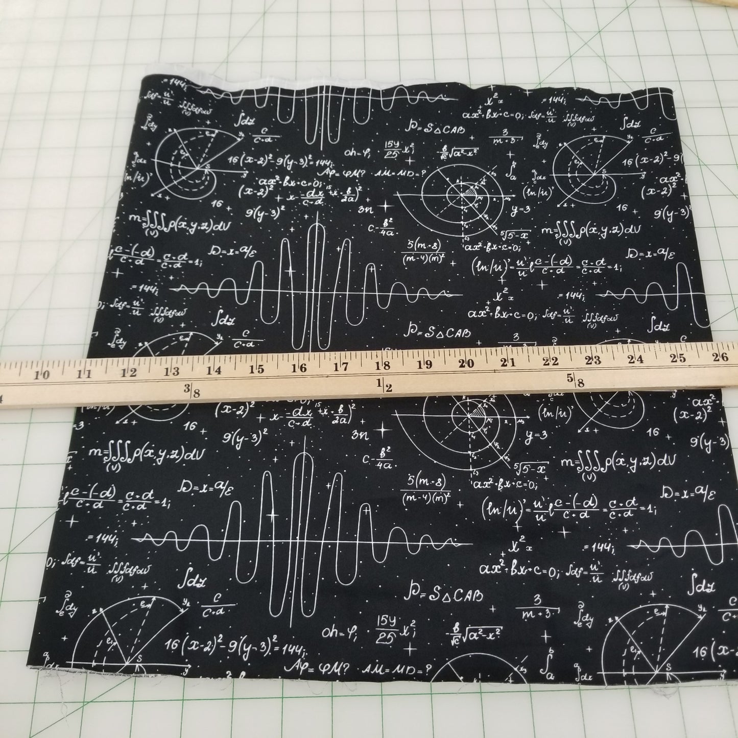 Black fabric with white mathematical equations and a ruler for scale on a grid background
