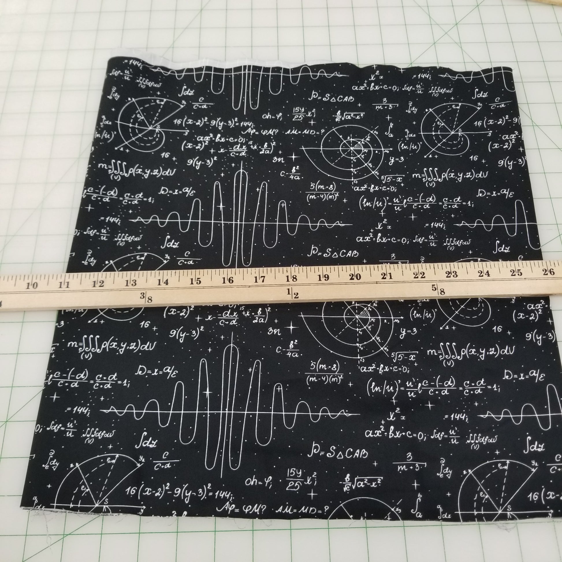 Black fabric with white mathematical equations and a ruler for scale on a grid background