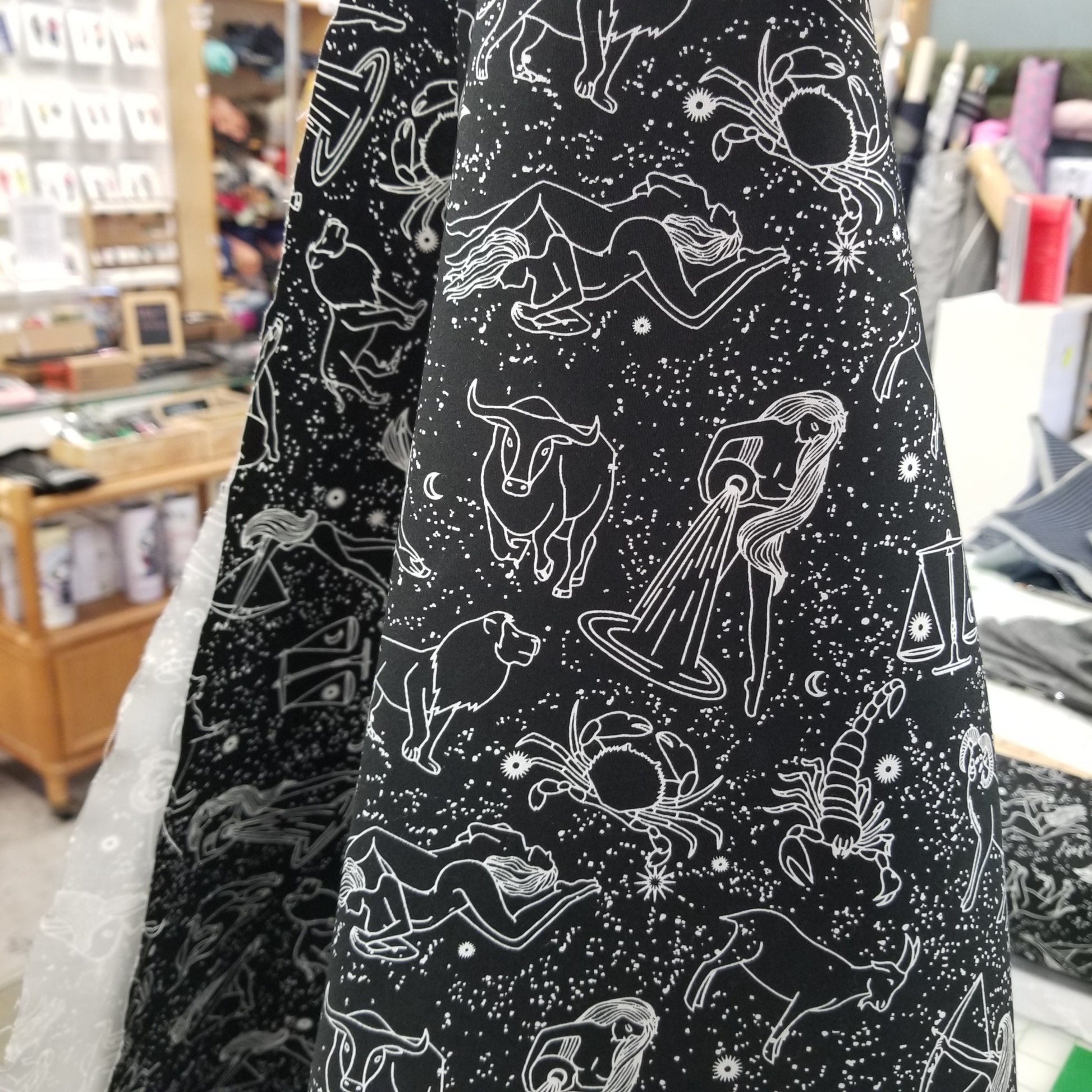 Black fabric with white zodiac constellation patterns, blurred store background
