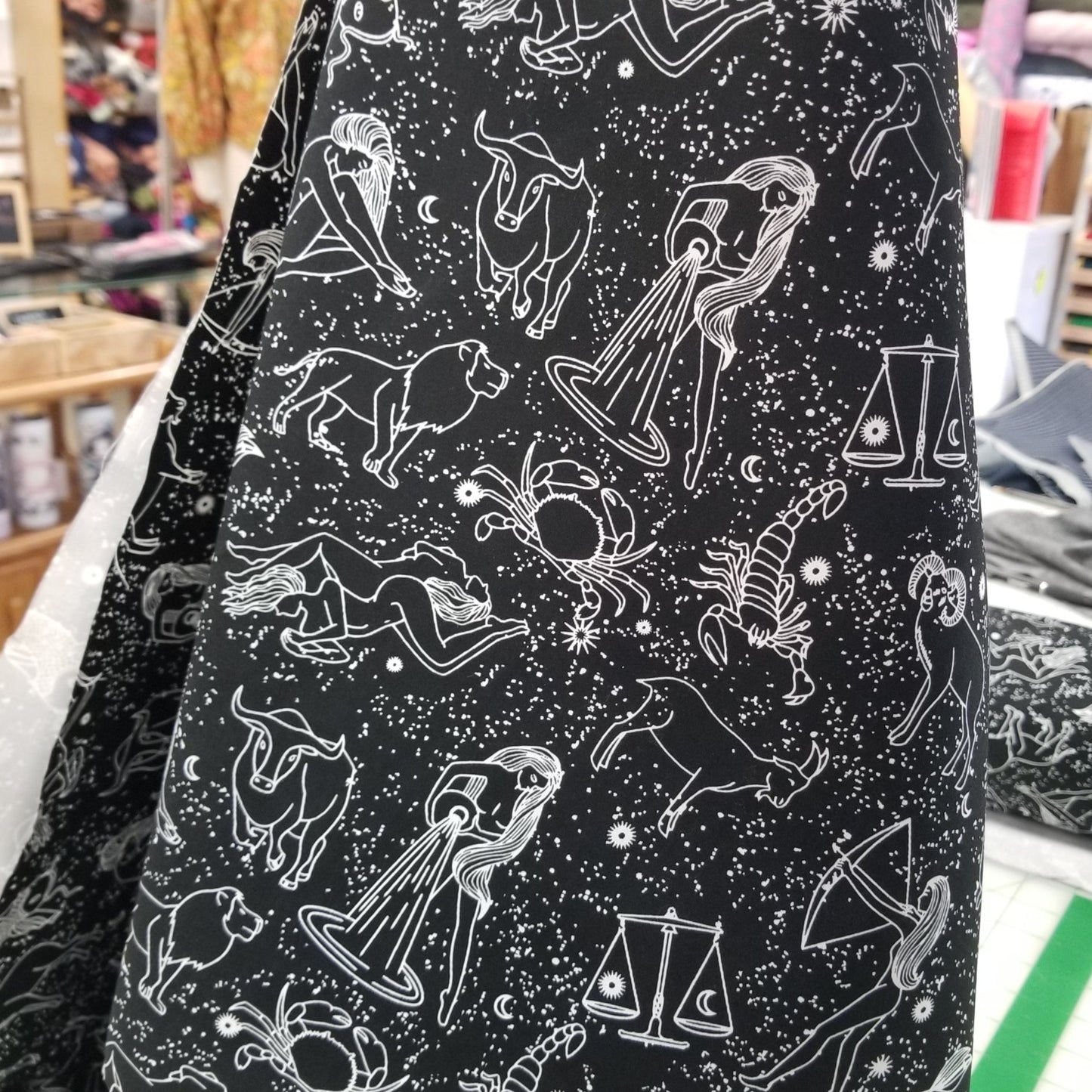 Black fabric with white zodiac constellation patterns, displayed in a store setting.