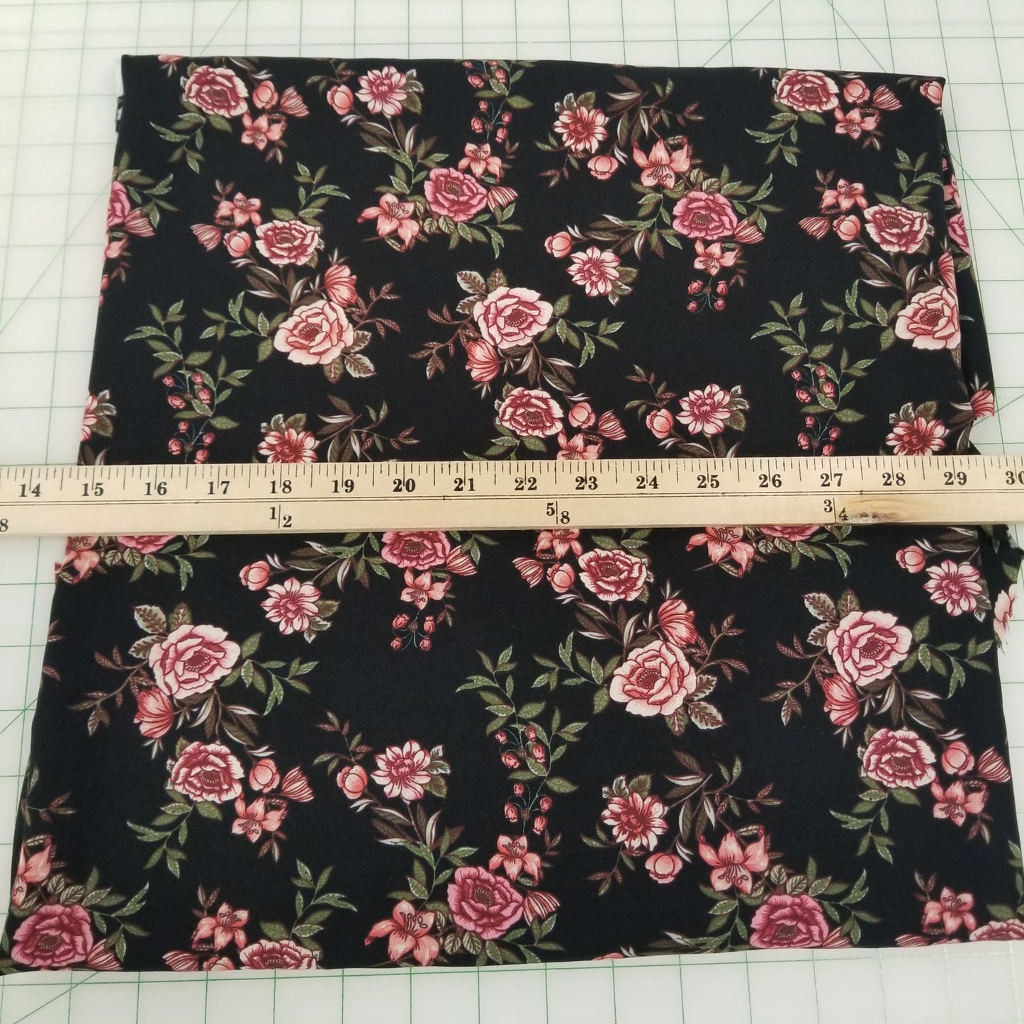 Floral fabric with pink flowers on a black background, measured with a ruler.