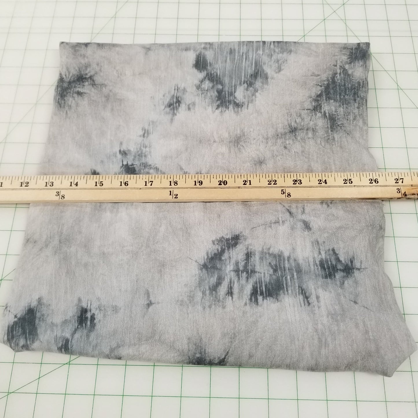 Gray tie-dye fabric on a white grid background with a ruler for scale.