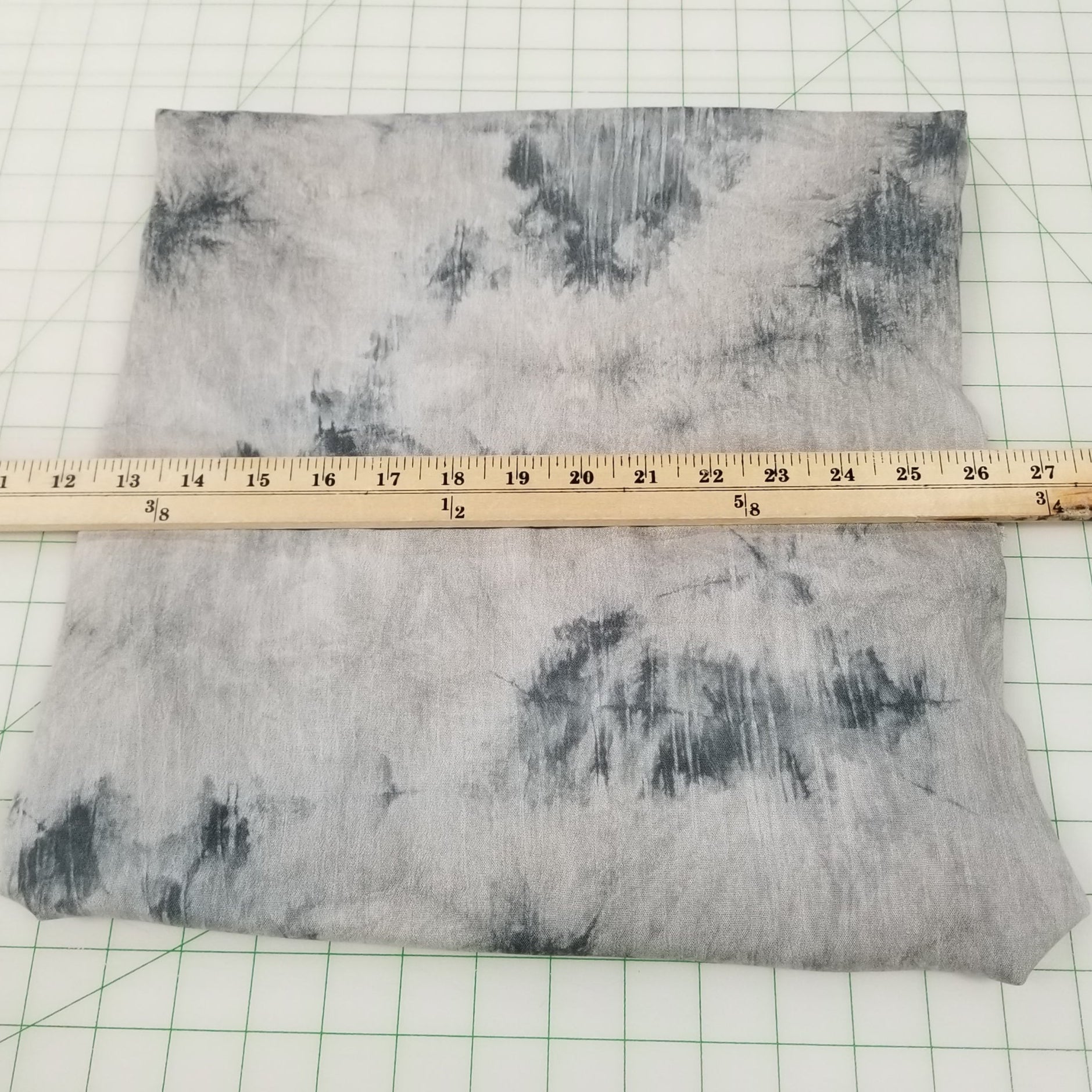 Gray tie-dye fabric on a white grid background with a ruler for scale.