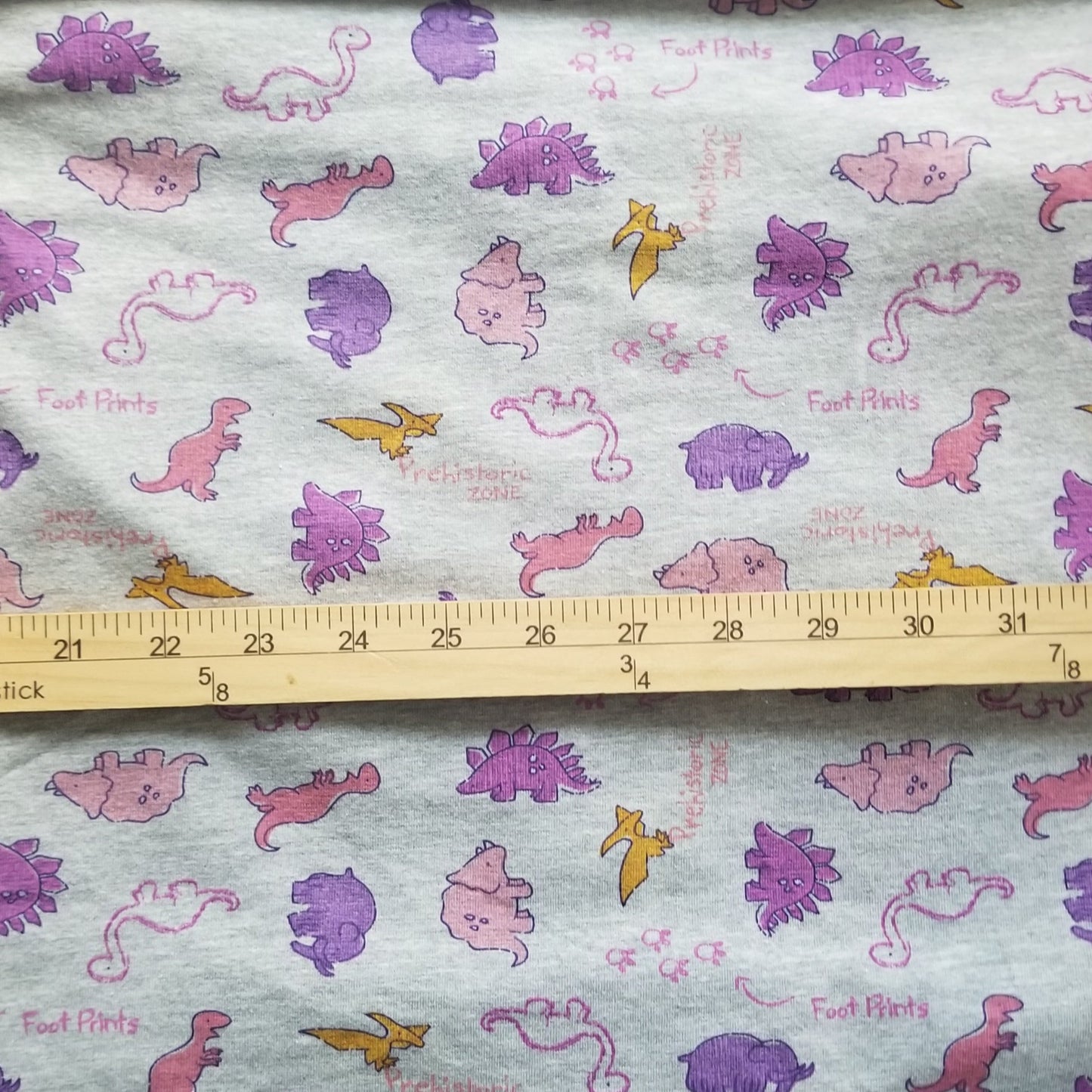 Fabric with dinosaur pattern and a ruler for scale on a wooden surface