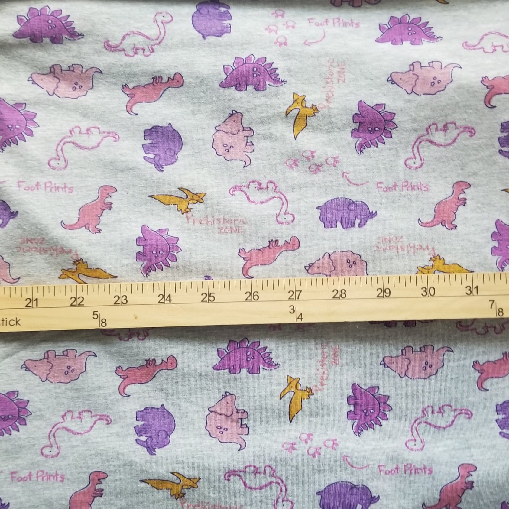 Fabric with dinosaur pattern and a ruler for scale on a wooden surface