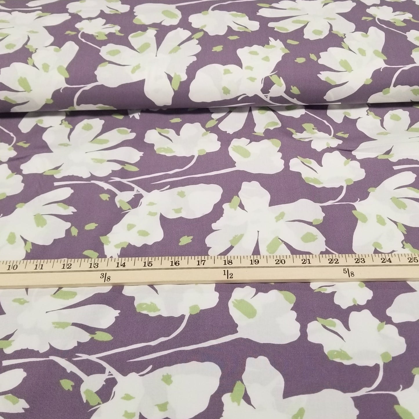 Floral fabric with white flowers on a purple background, measured with a ruler.
