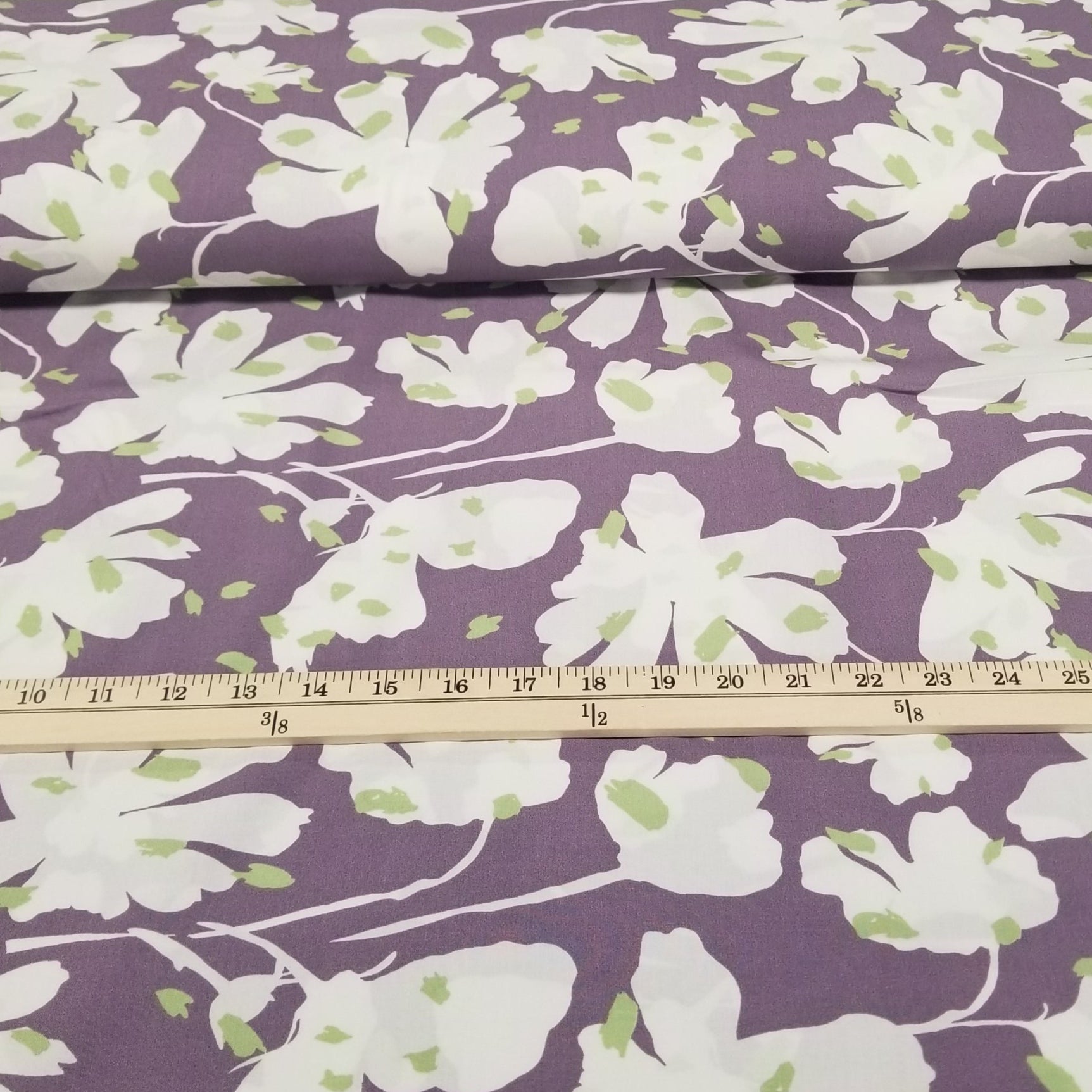 Floral fabric with white flowers on a purple background, measured with a ruler.