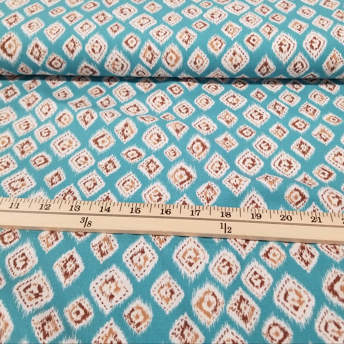 Fabric with a diamond pattern on a blue background, measured by a ruler.