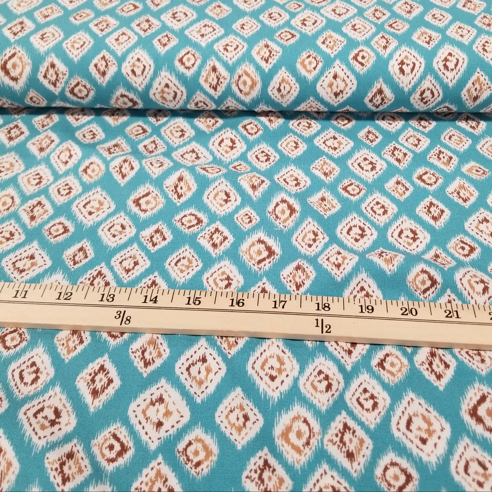 Fabric with a diamond pattern on a blue background, measured by a ruler.