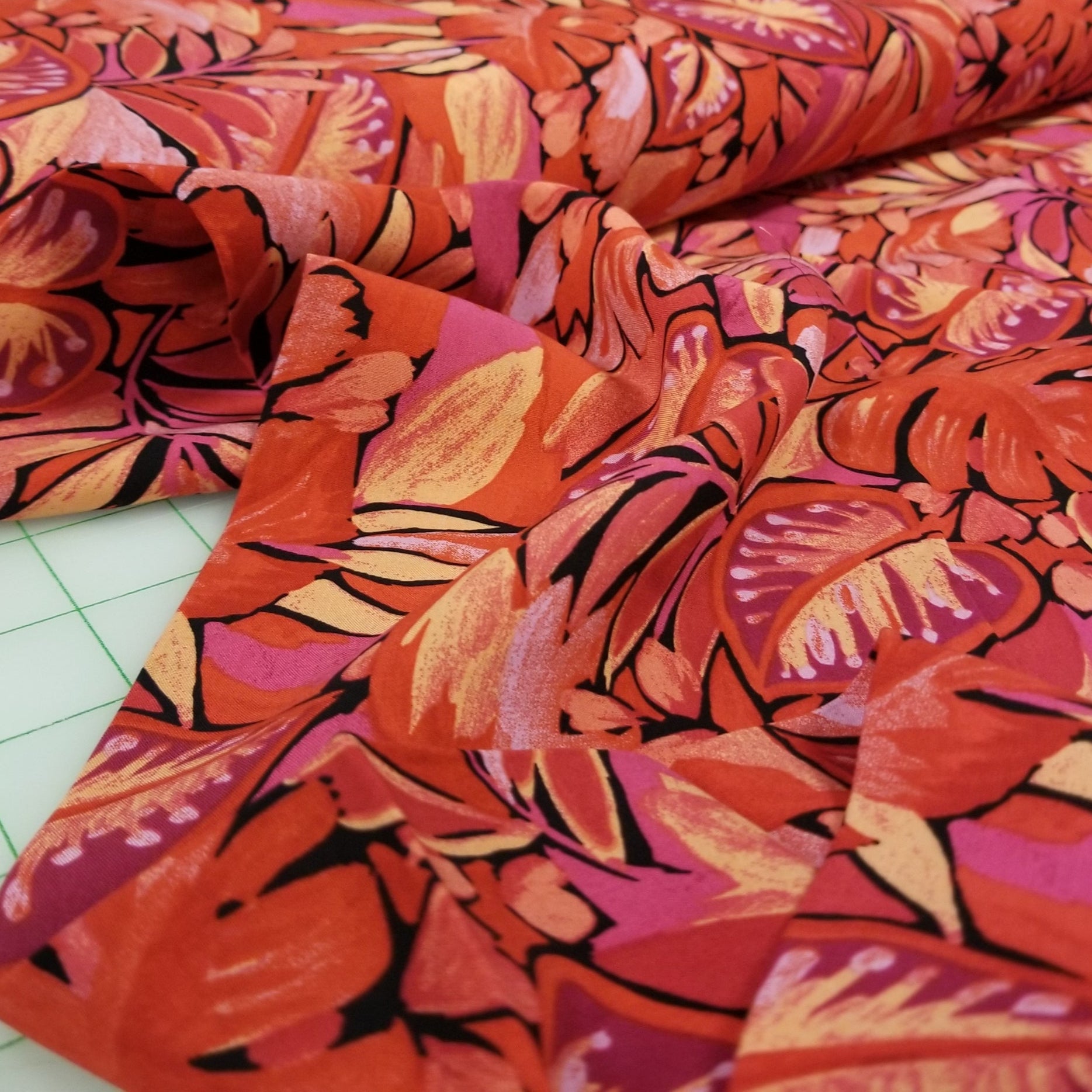 Close-up of vibrant red and pink floral fabric on a cutting mat.