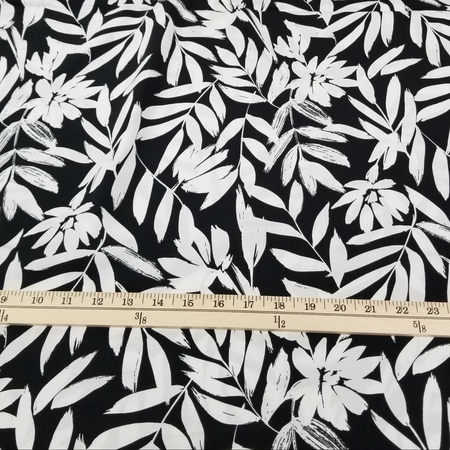 Fabric with white leaf pattern on black background, measured by a ruler.