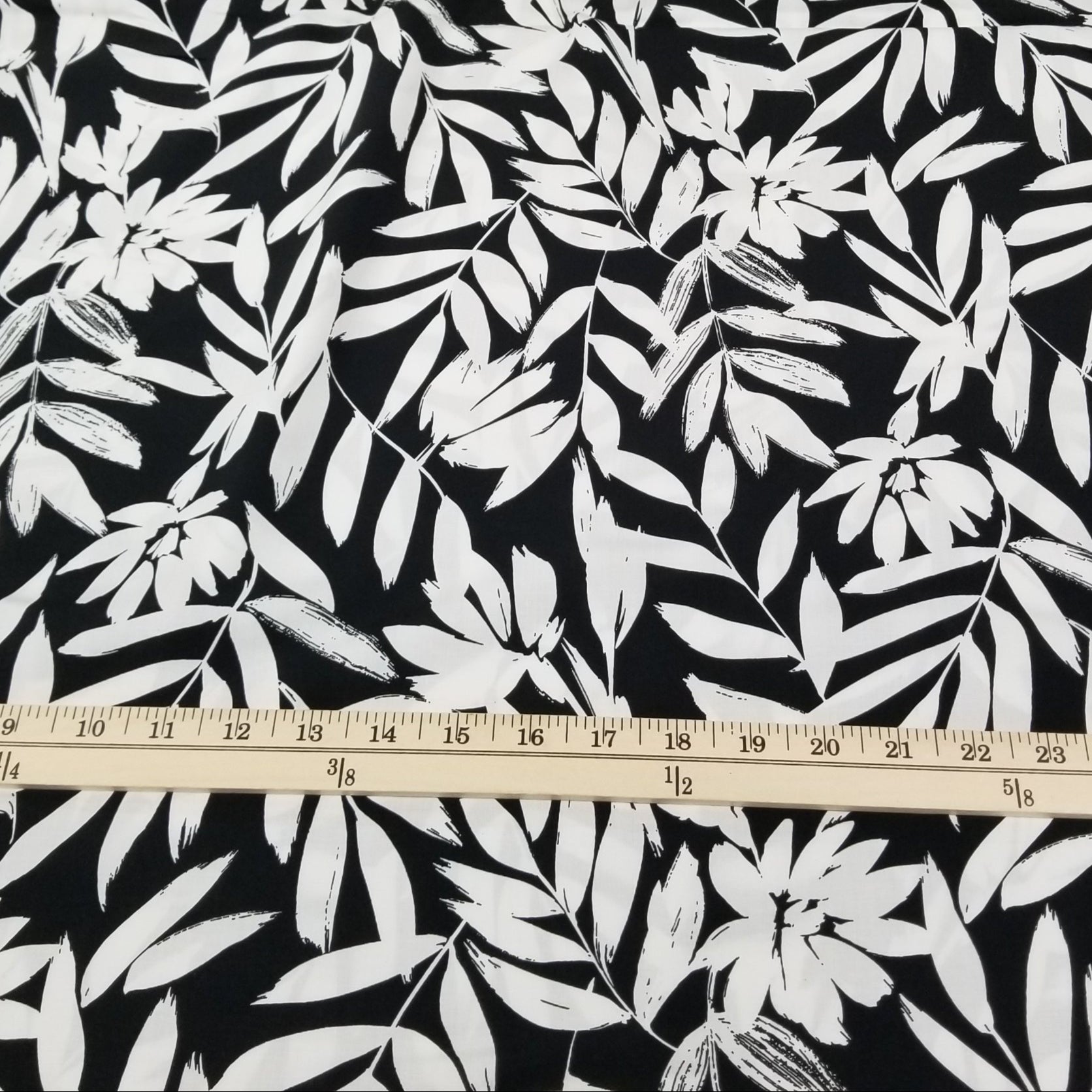Fabric with white leaf pattern on black background, measured by a ruler.