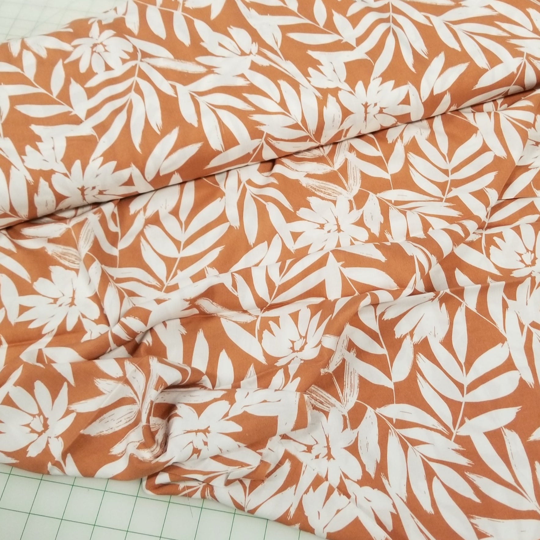 Fabric with white leaf pattern on orange background on a grid surface