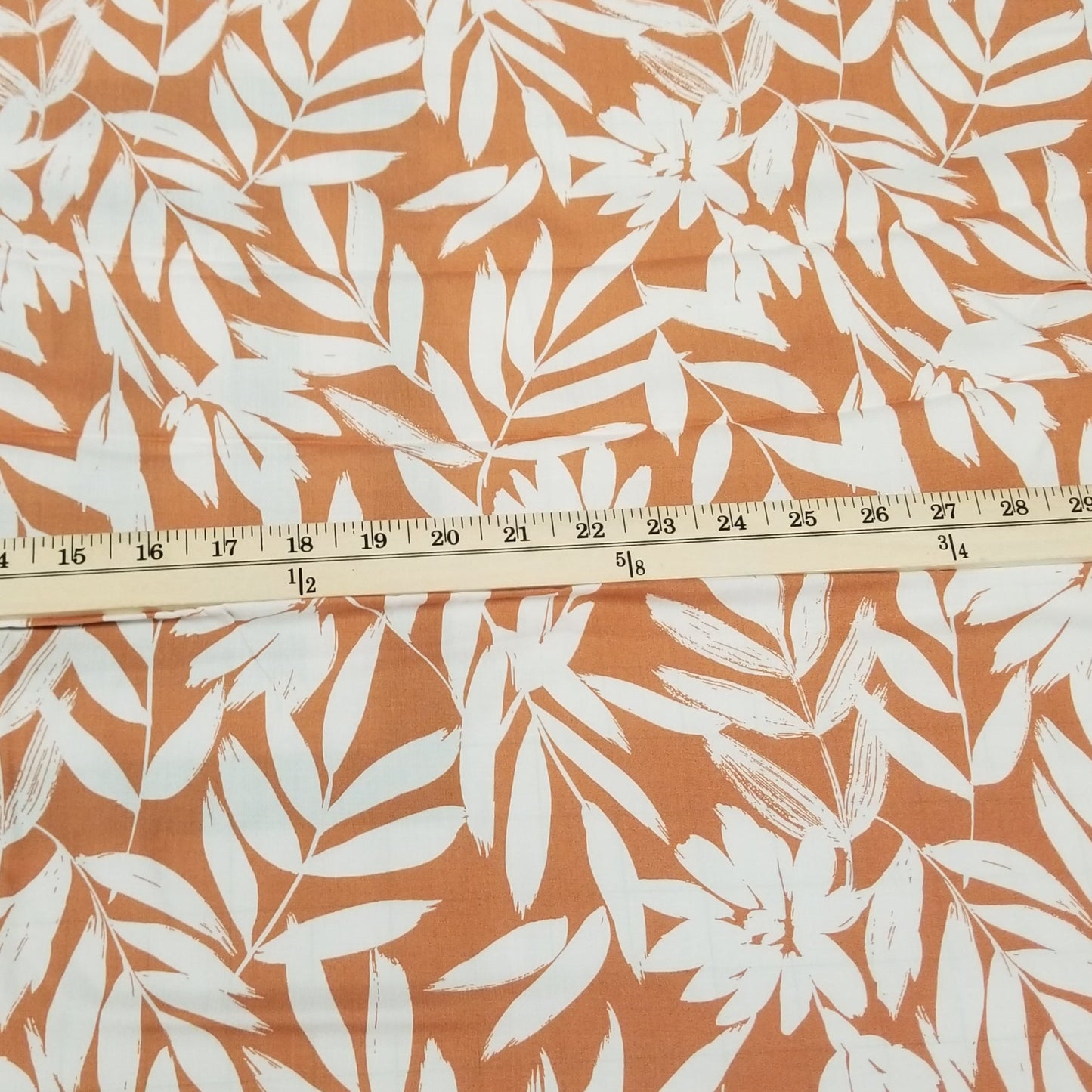 Fabric with white leaf pattern on an orange background, measured with a ruler.