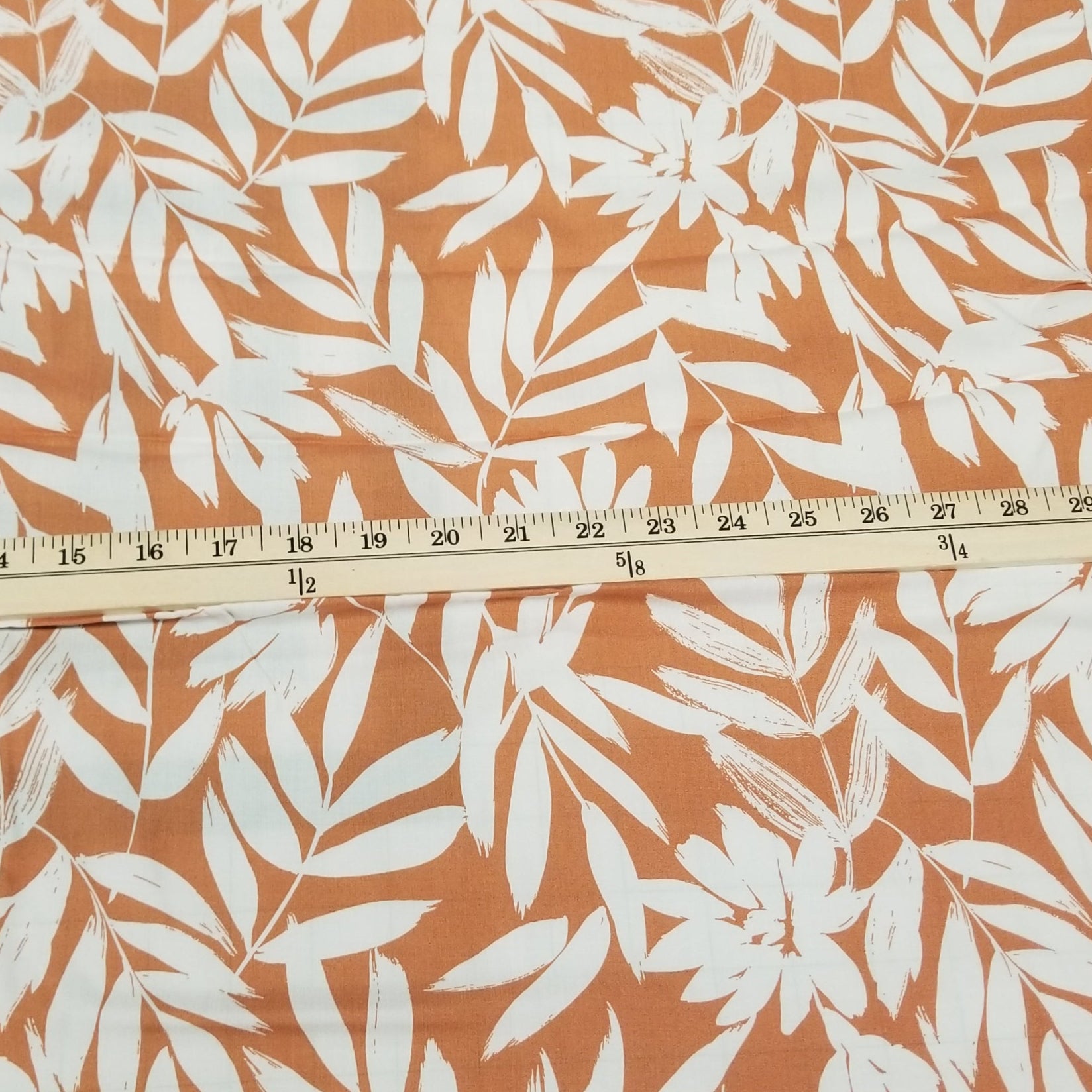 Fabric with white leaf pattern on an orange background, measured with a ruler.