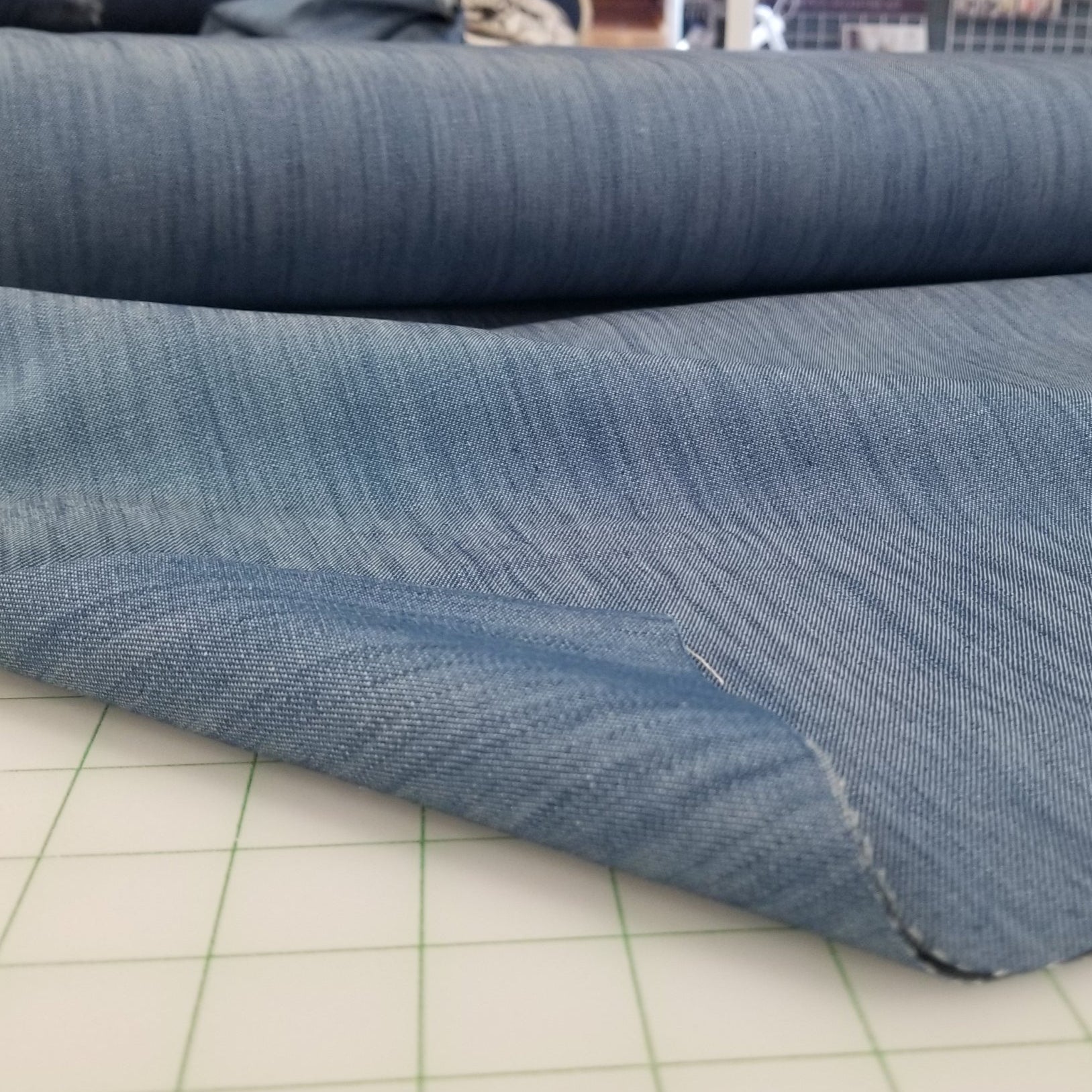Close-up of blue fabric on a cutting mat with sewing equipment in the background
