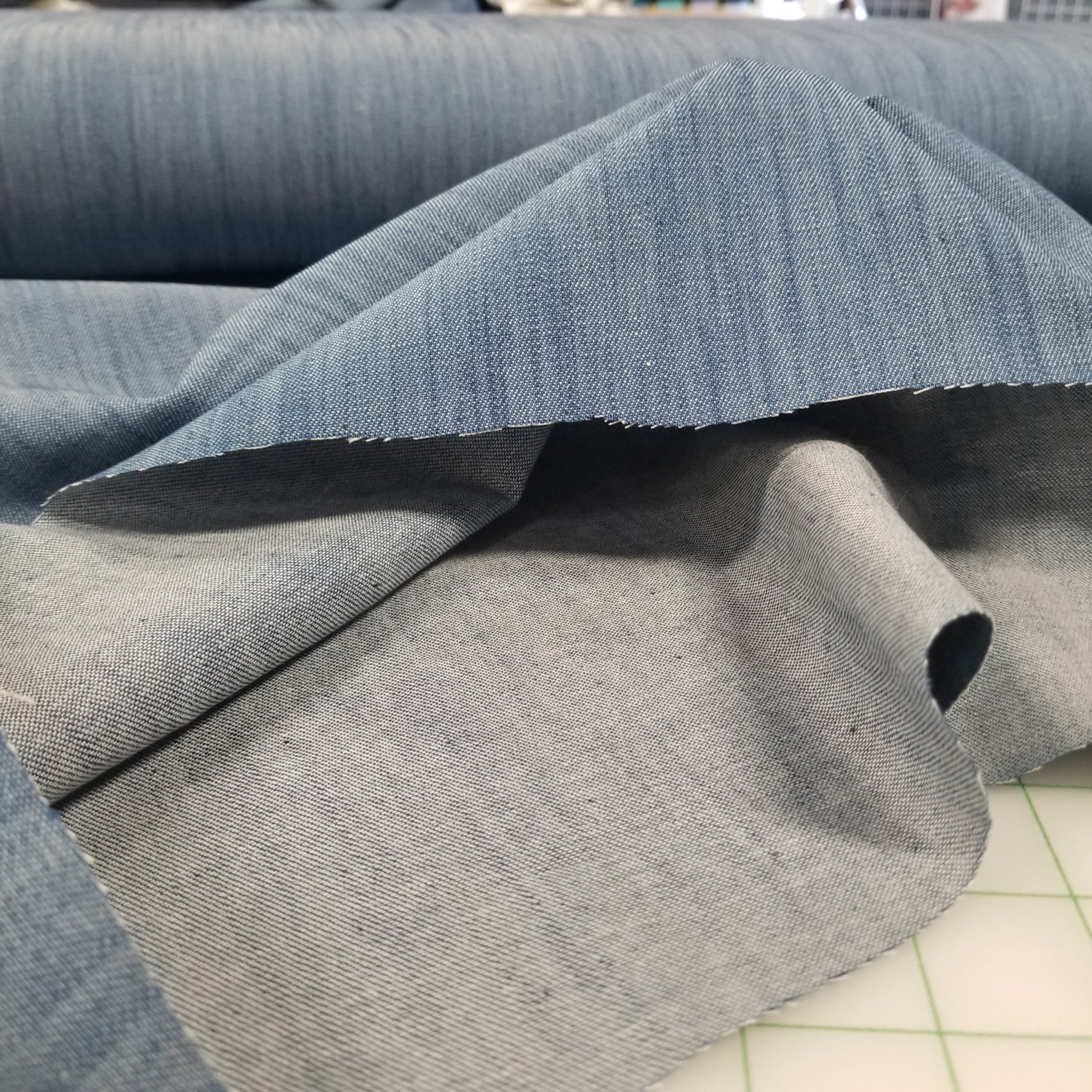 Close-up of gray fabric with a visible seam on a cutting mat.