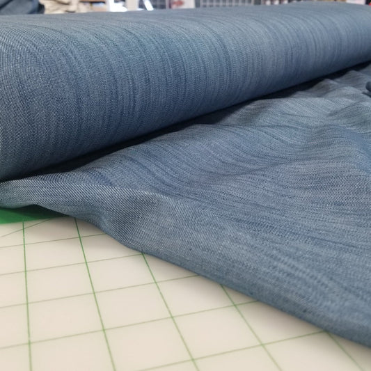 Roll of blue fabric on a cutting mat with a store setting in the background