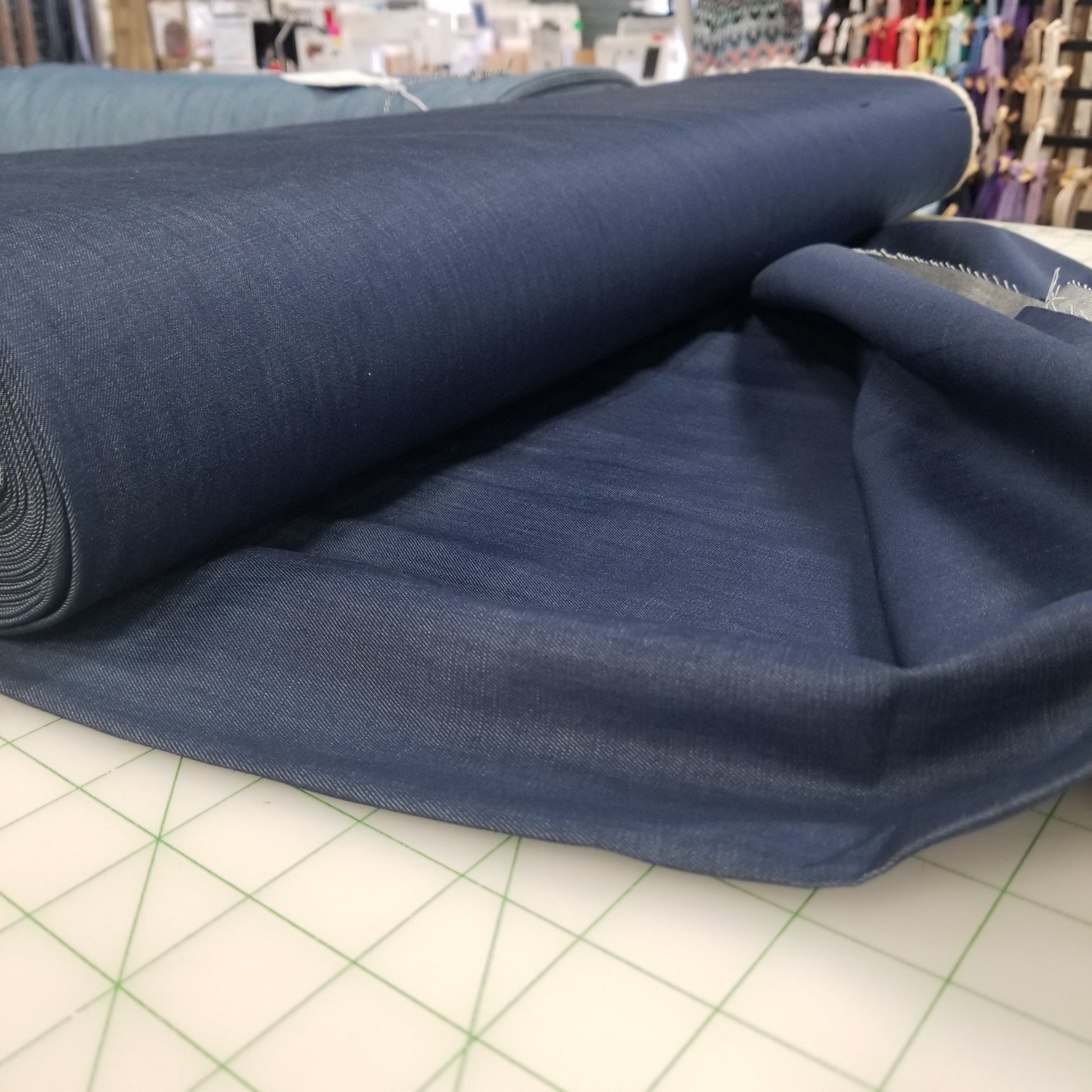 Roll of blue fabric on a cutting mat with a fabric store in the background