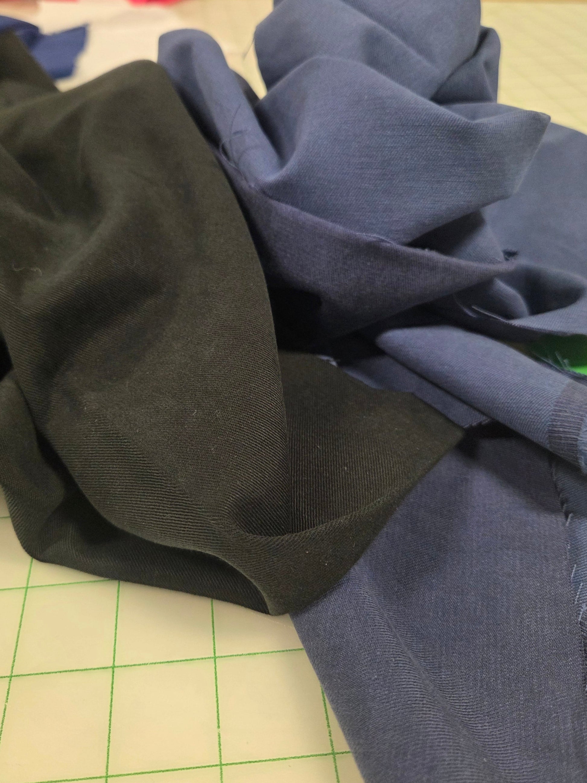 Stack of black and blue fabric on a grid surface. tencel cotton twill solids