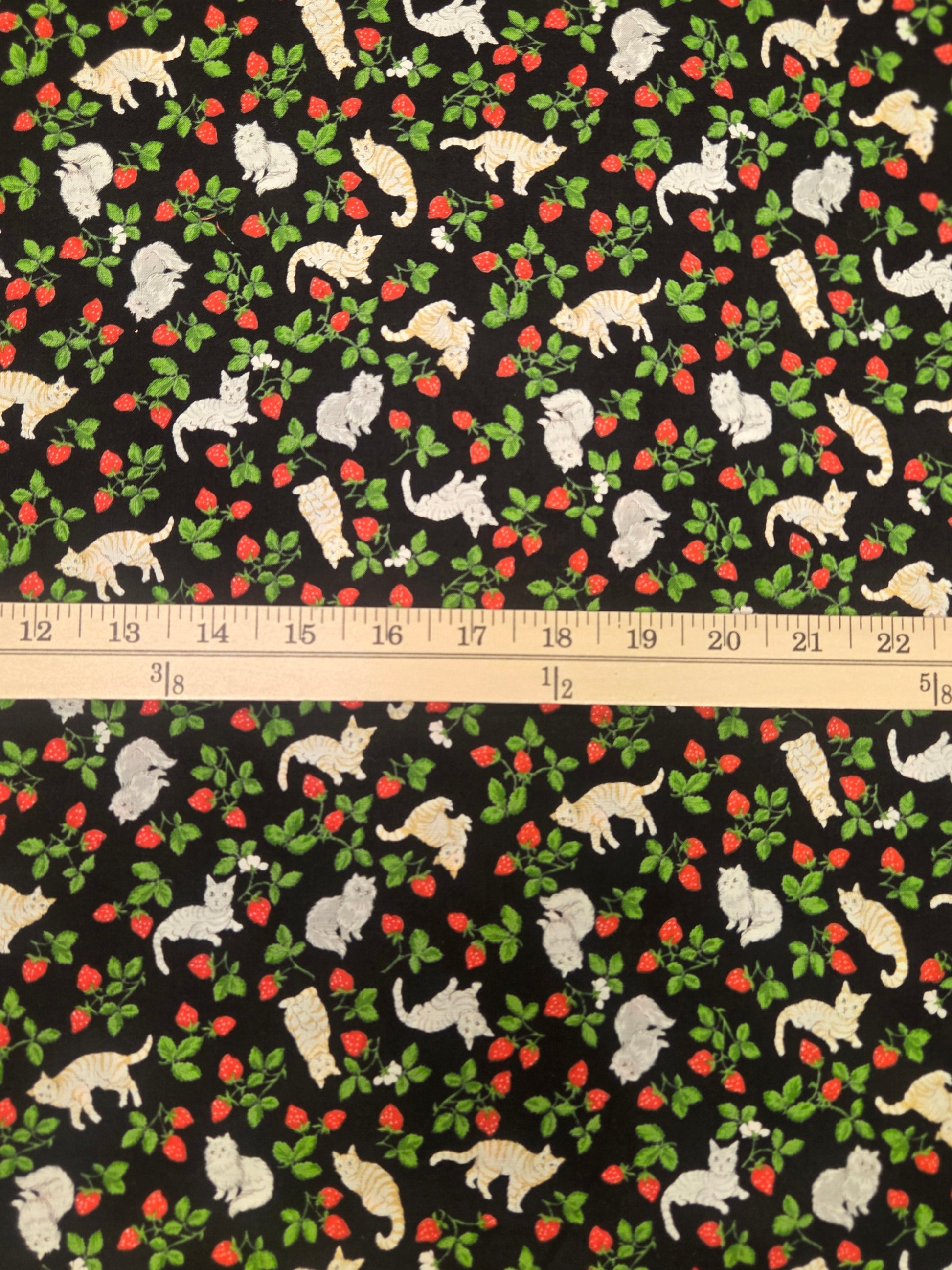 Fabric with a pattern of white animals and red berries on a black background, with a ruler for scale.
