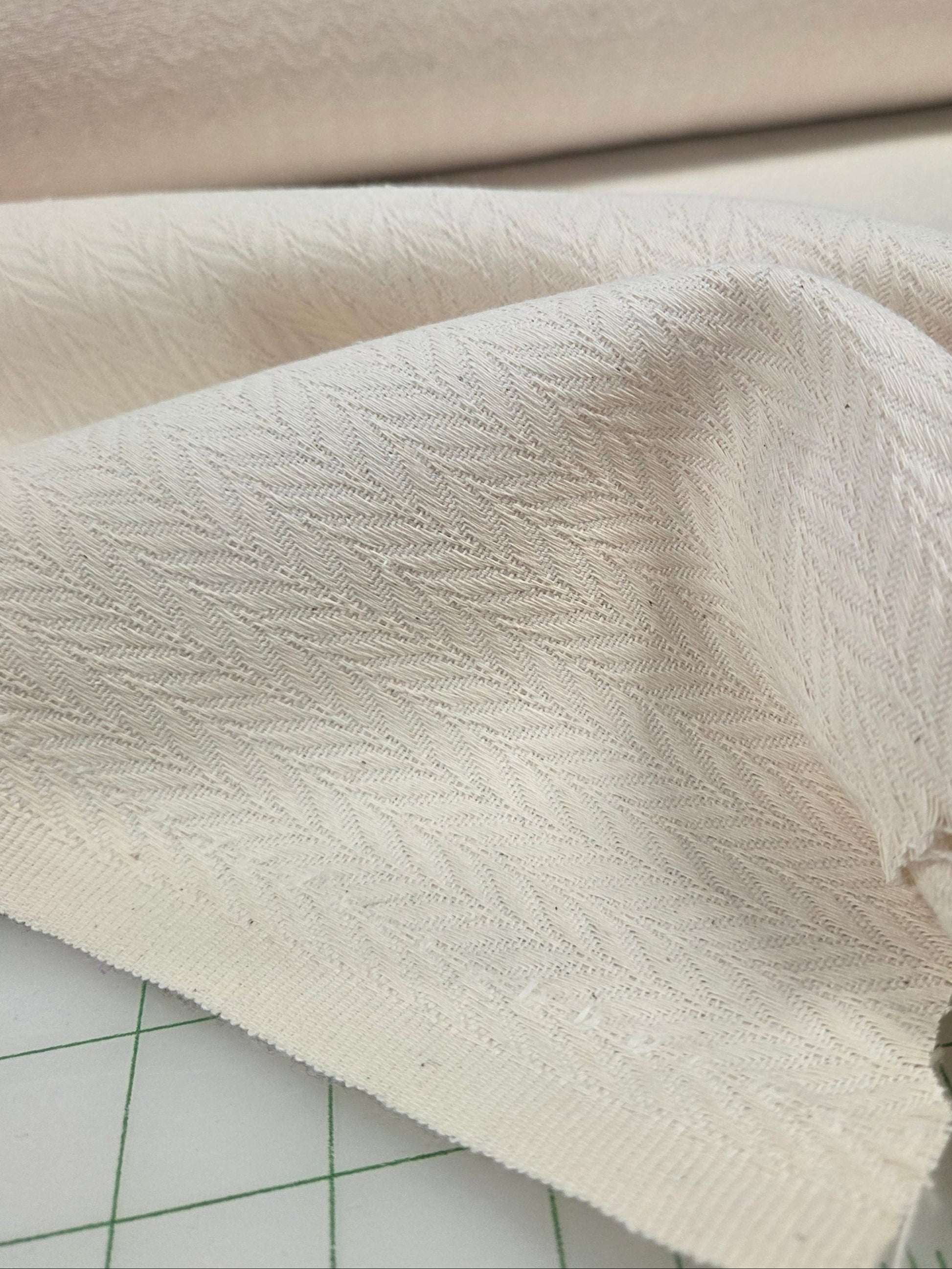 Close-up of textured cream herringbone fabric on a cutting mat with ruler