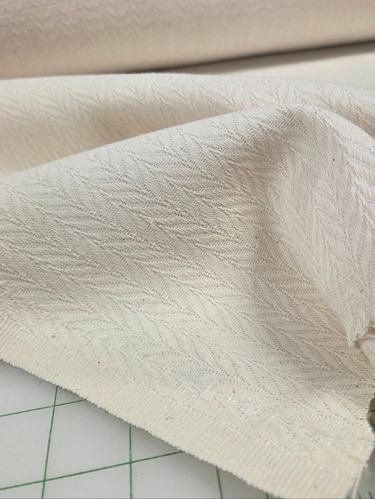 Close-up of textured cream herringbone fabric on a cutting mat with ruler
