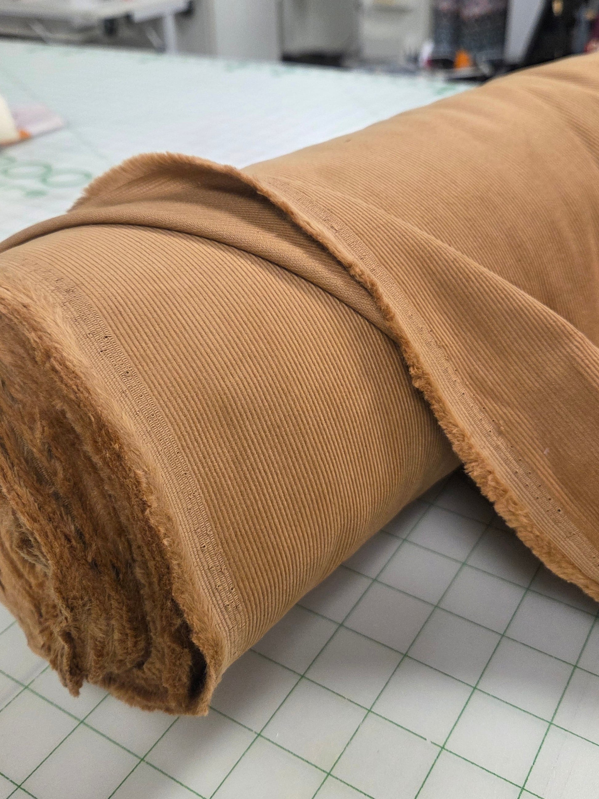 Roll of brown fabric on a grid surface with a store background. camel cotton corduroy. LA Finch Fabric by the yard