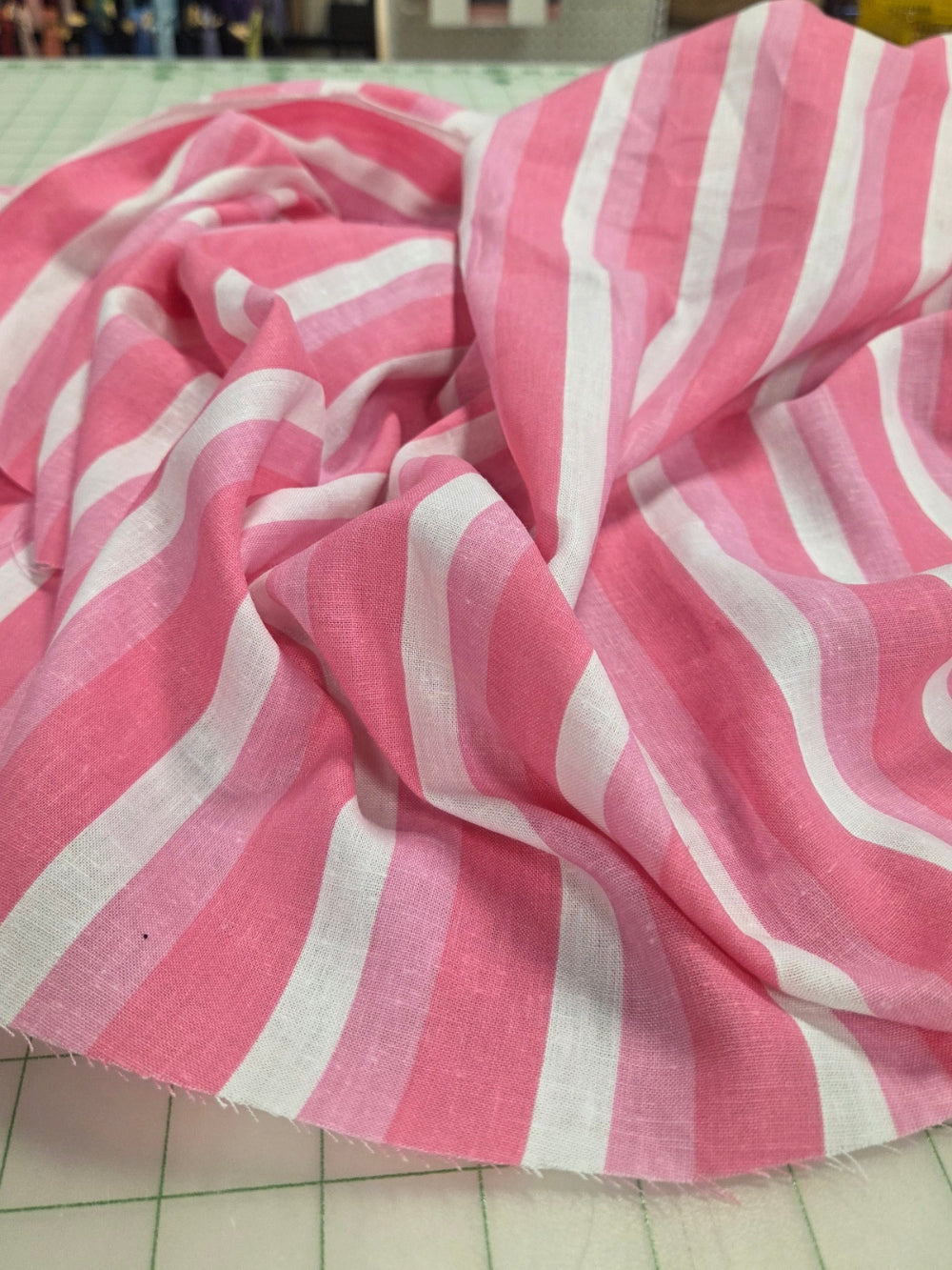 Pink and white striped fabric on a tiled floor with a store background. stripe fabric designer deadstock woven. fabric by the yard. Cali Fabrics in store and online LA Finch Fabrics. LA fabric.