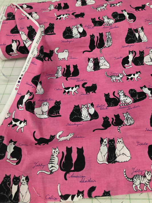 Fabric with black and white cat pattern on a pink background, displayed on a cutting mat.