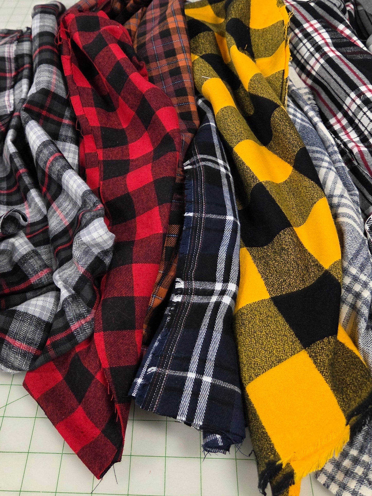 Stack of plaid fabrics in various colors on a cutting mat.