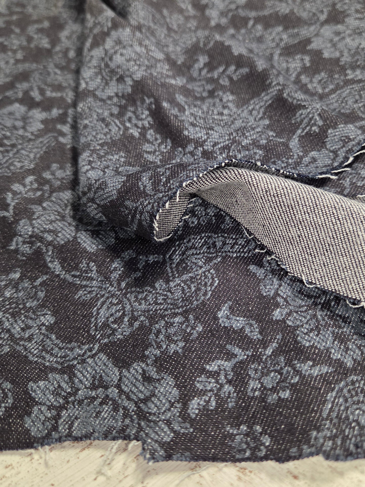 Close-up of a textured fabric with a floral pattern on a neutral background. Italian cotton denim printed paisley woven