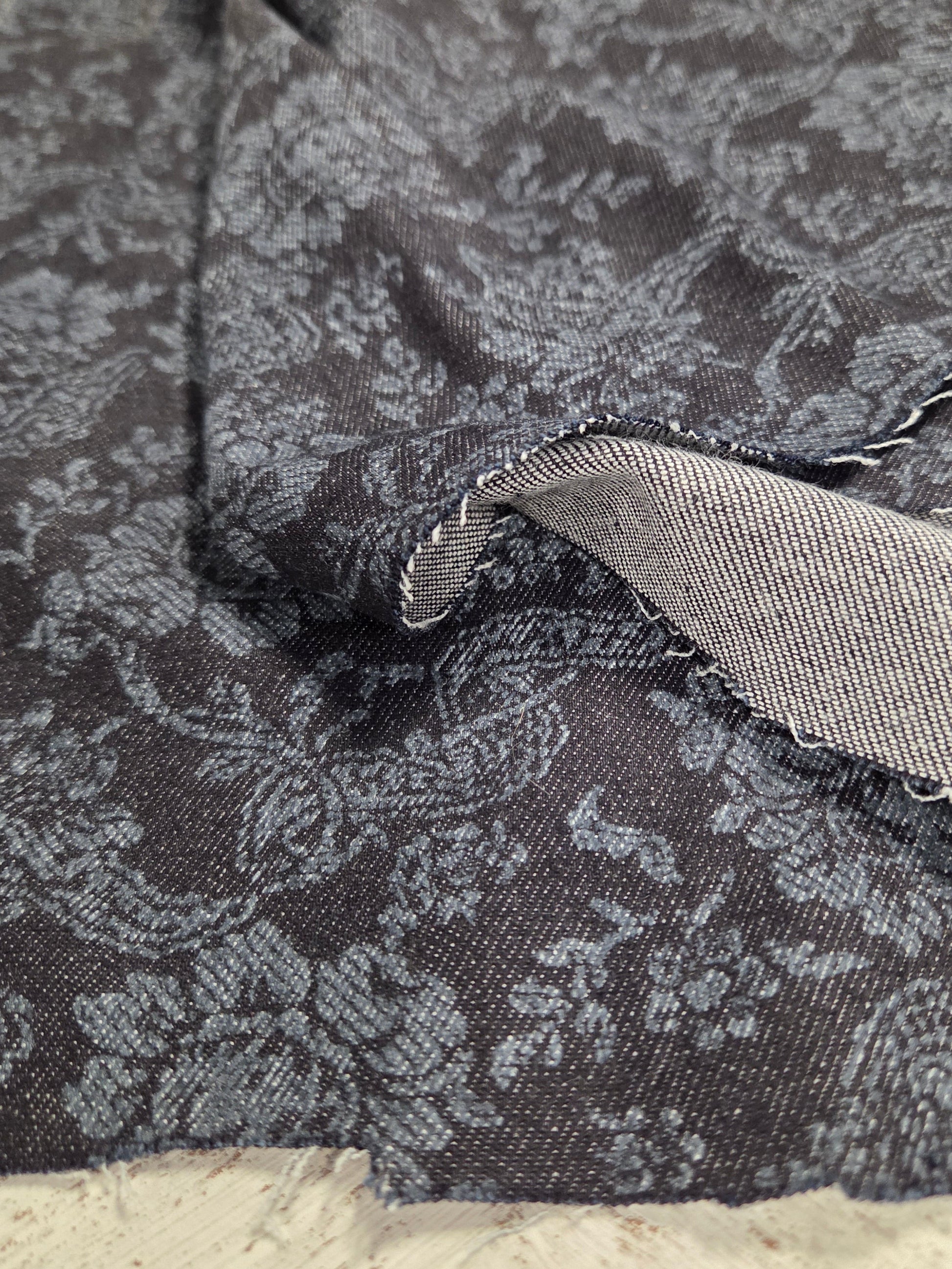 Close-up of a textured fabric with a floral pattern on a neutral background. Italian cotton denim printed paisley woven