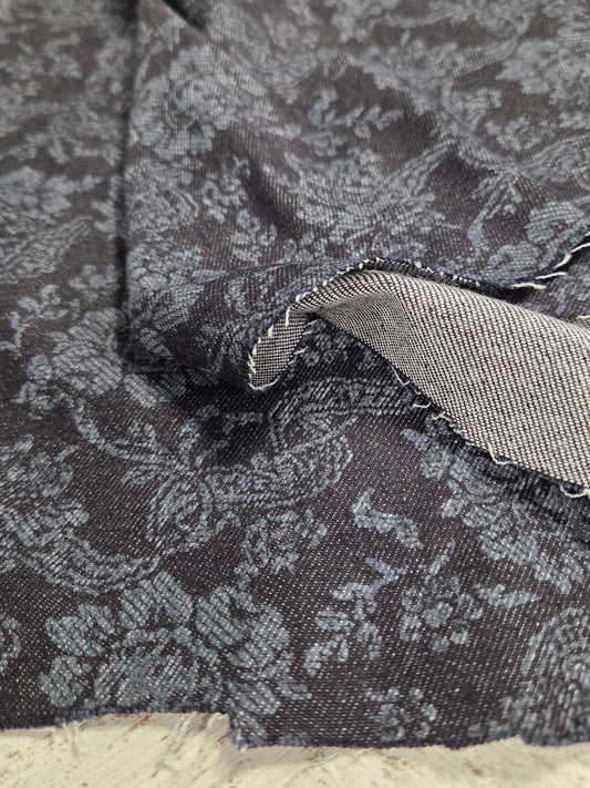 Close-up of a textured fabric with a floral pattern on a neutral background. Italian cotton denim printed paisley woven