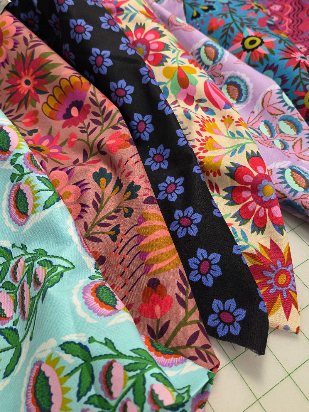 Colorful fabric samples with floral patterns on a cutting mat.