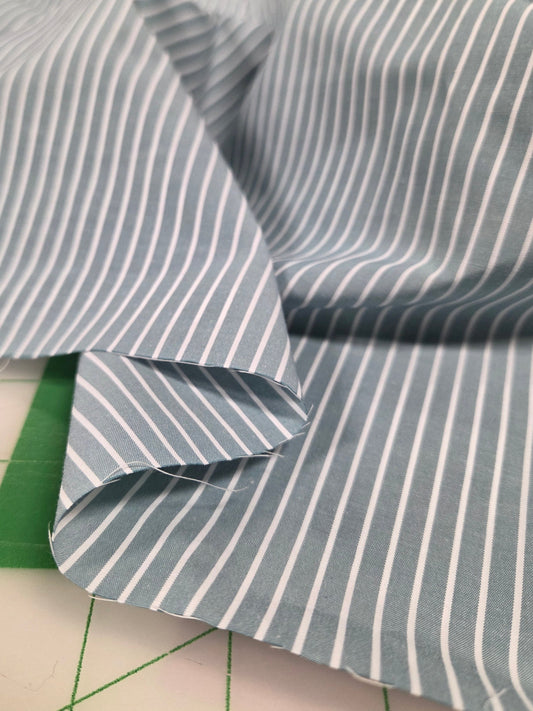 sage green and white striped fabric on a cutting mat with grid lines. cotton shirting poplin. deadstock