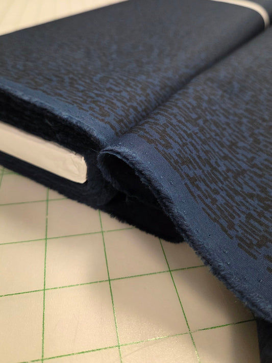 Close-up of blue textured fabric on a cutting mat with blurred background