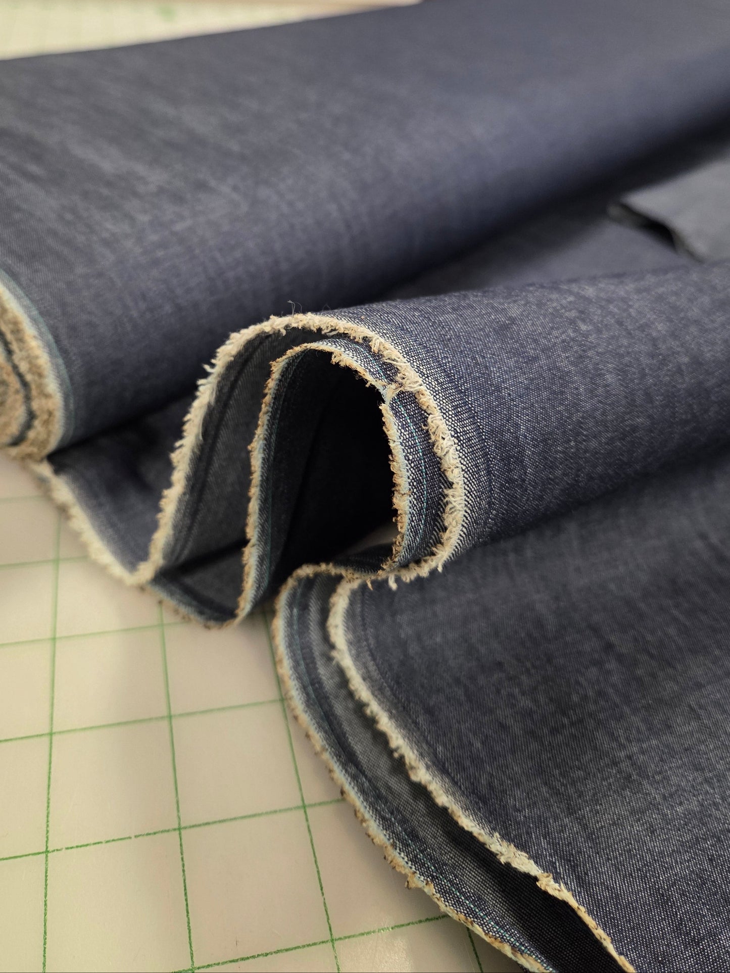 Roll of denim fabric on a cutting mat with a blurred background. sold and priced by the yard. apparel fabrics for sewing. Online fabric shopping chambray solid wovens