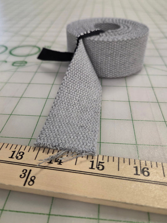 Roll of gray fabric with a ruler for scale on a grid background. webbing 3 yard precuts