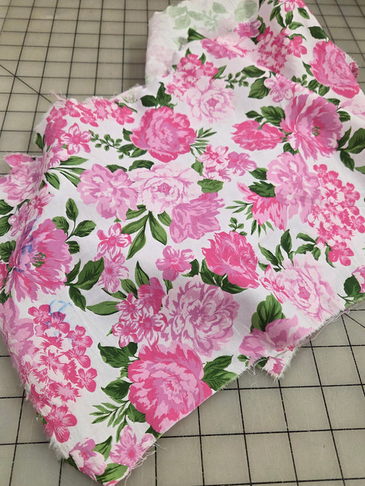Floral fabric with pink flowers on a white background, placed on a grid surface. Cotton Spandex Poplin sold by the yard. Retail in southern california. Cottage core pink roses with various shades of pink