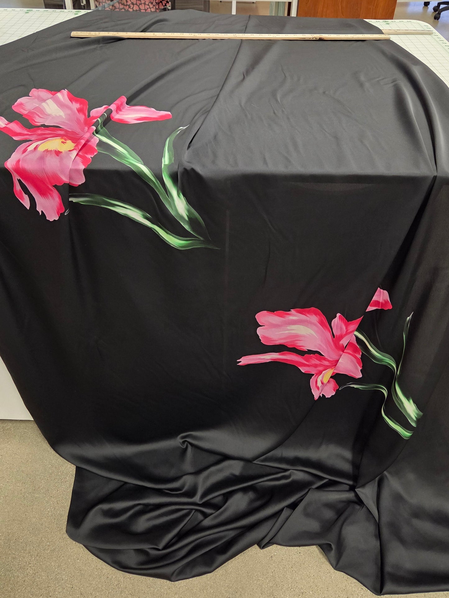 Black fabric with pink floral designs on a stand in a store setting