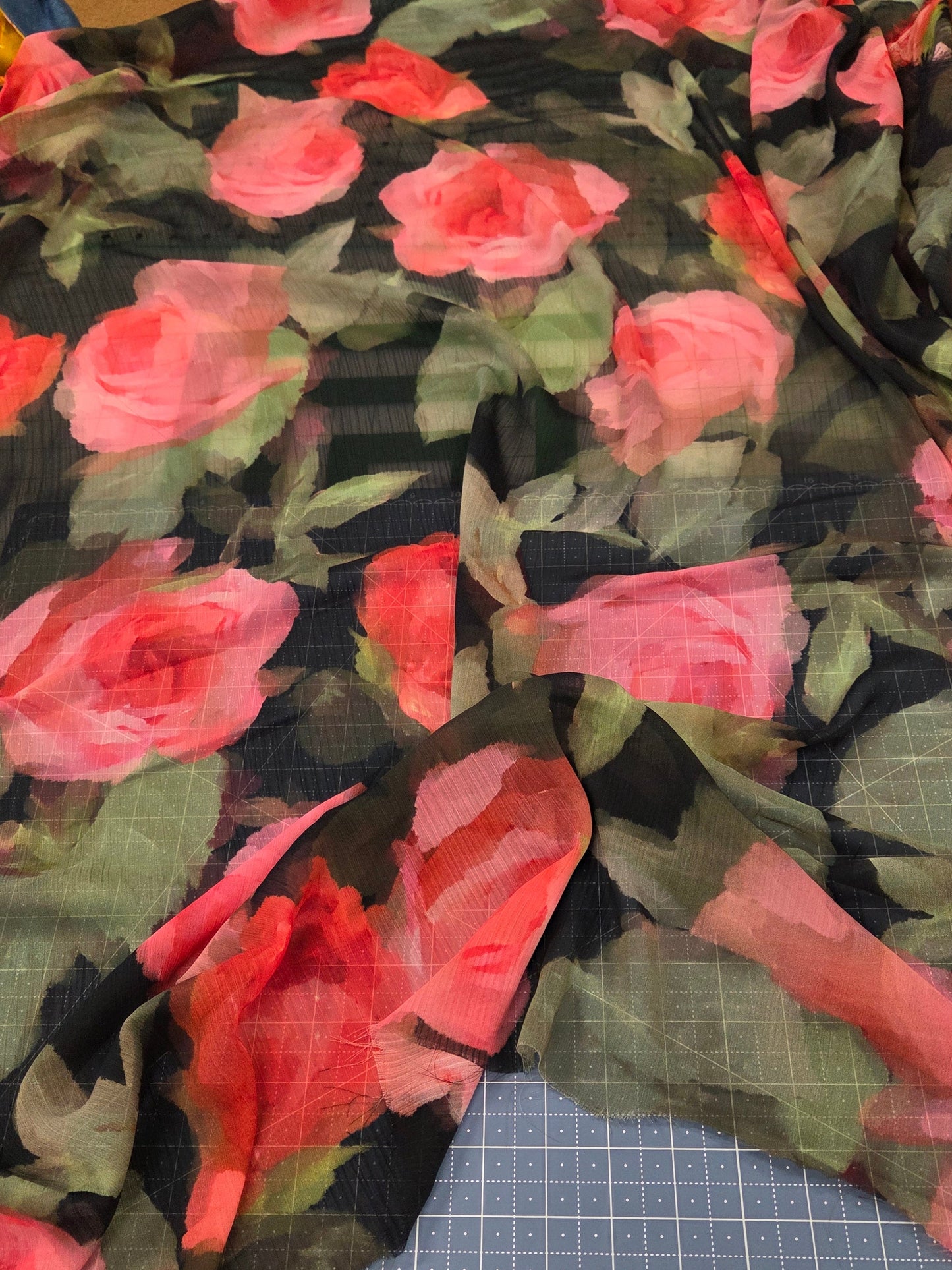 Floral fabric with pink roses on a black background, cut and displayed on a cutting mat.