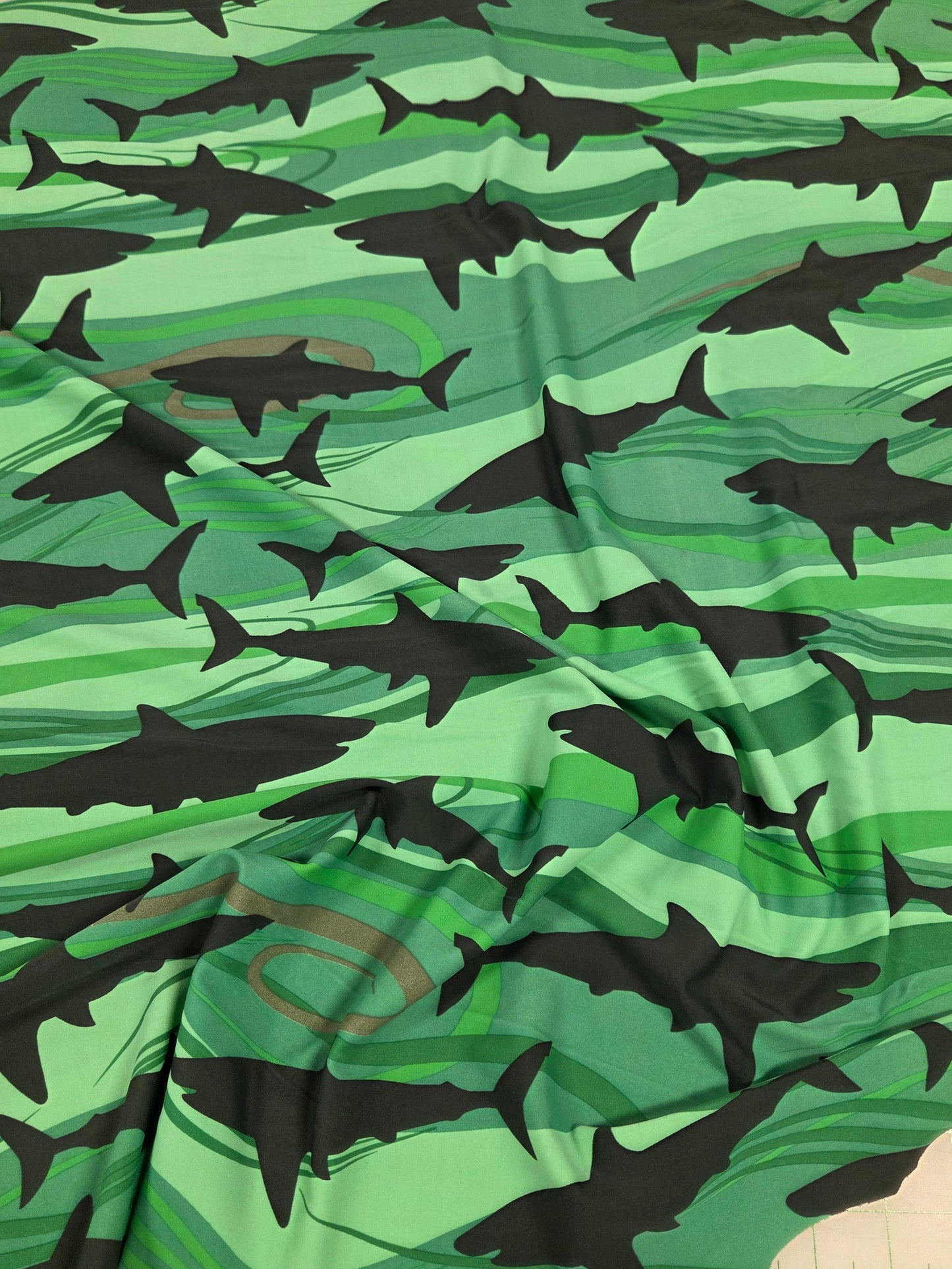 Fabric with shark pattern on a green background, measured against a ruler.