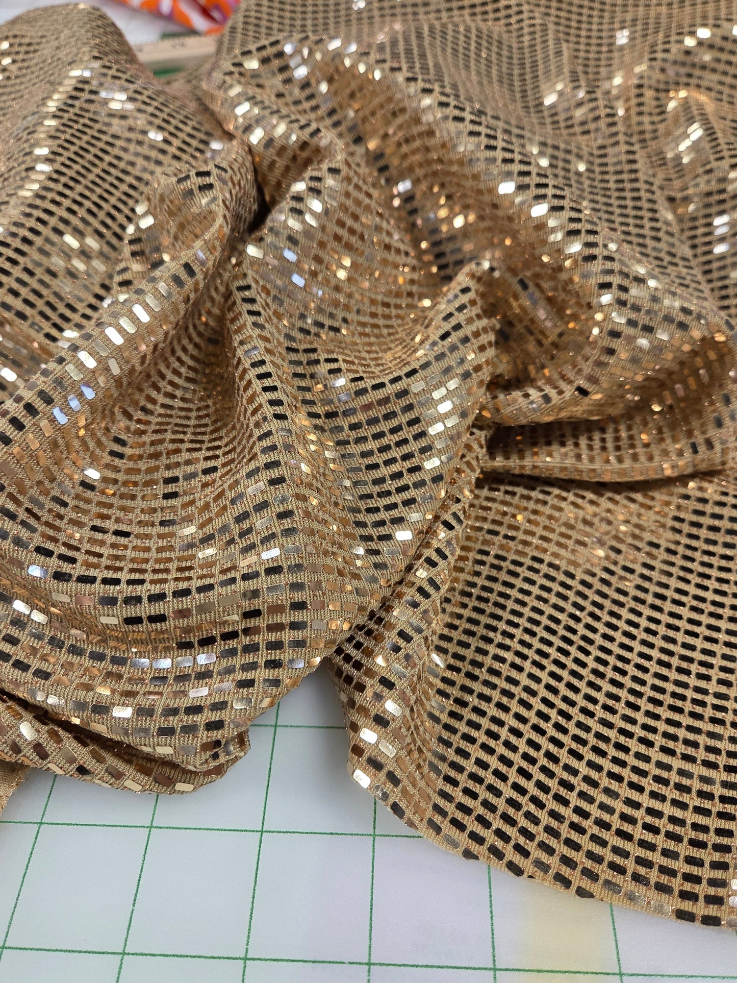 Close-up of gold sequin fabric on a white surface with grid lines