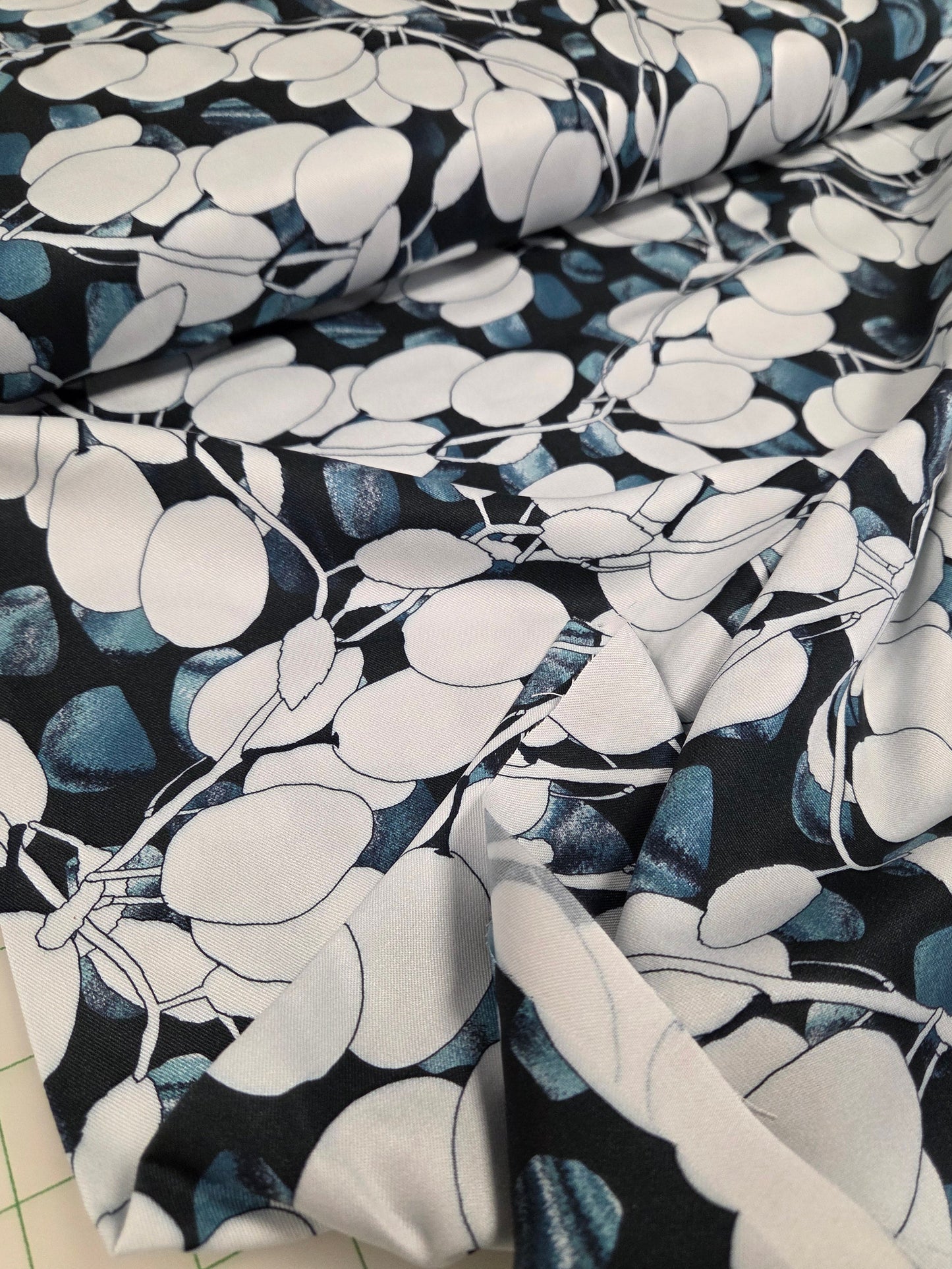 Fabric with a black, white, and blue floral pattern on a cutting mat. Stof Fabrics,Denmark, viscose twill rayon opaque