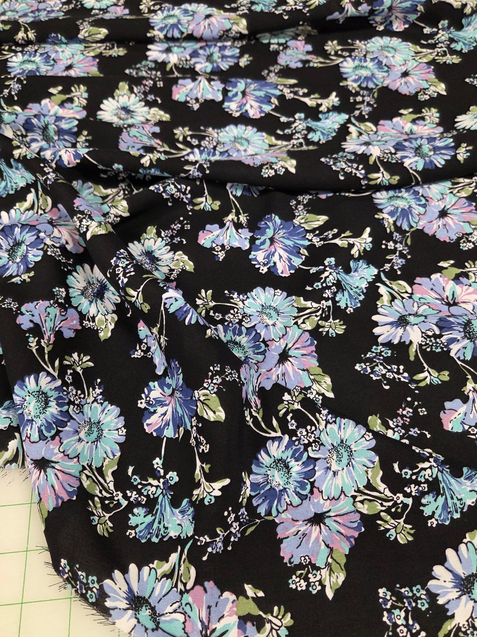 Floral fabric with blue and purple flowers on a black background, laid out on a grid surface.
