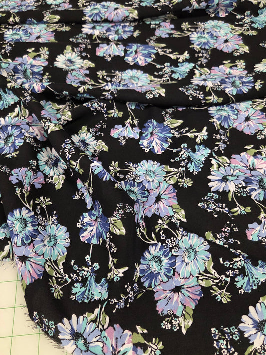 Floral fabric with blue and purple flowers on a black background, laid out on a grid surface.